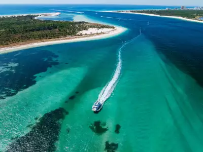 A boat jets through the emerald green waters and white sand of Panama City Beach in Florida, captured from above