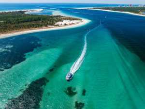 A boat jets through the emerald green waters and white sand of Panama City Beach in Florida, captured from above
