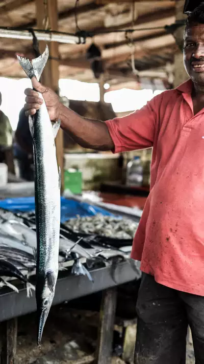 A man hoisting an usi kola fish at a market